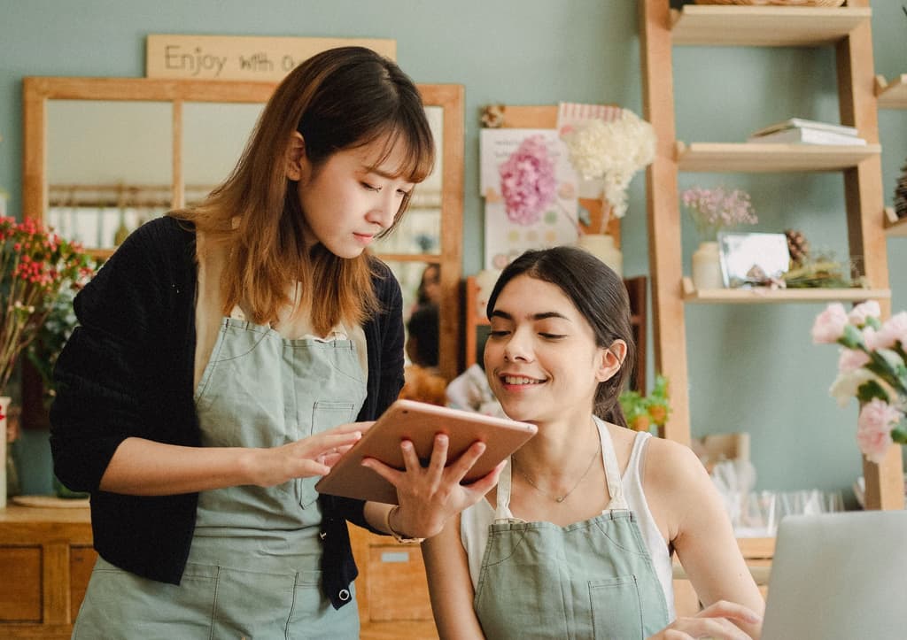 Two shop staff in aprons looking at a tablet together